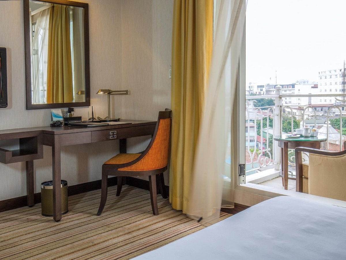 Executive room desk and orange armchair beside an open balcony door with Old Quarter rooftops outside