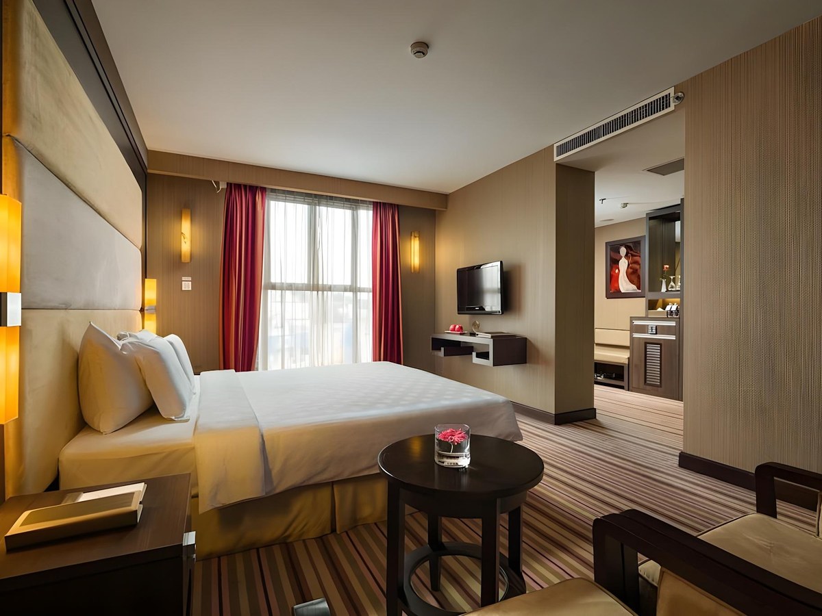 Premium Deluxe room with dark wood panelling, a high cream headboard, red curtains and a round side table