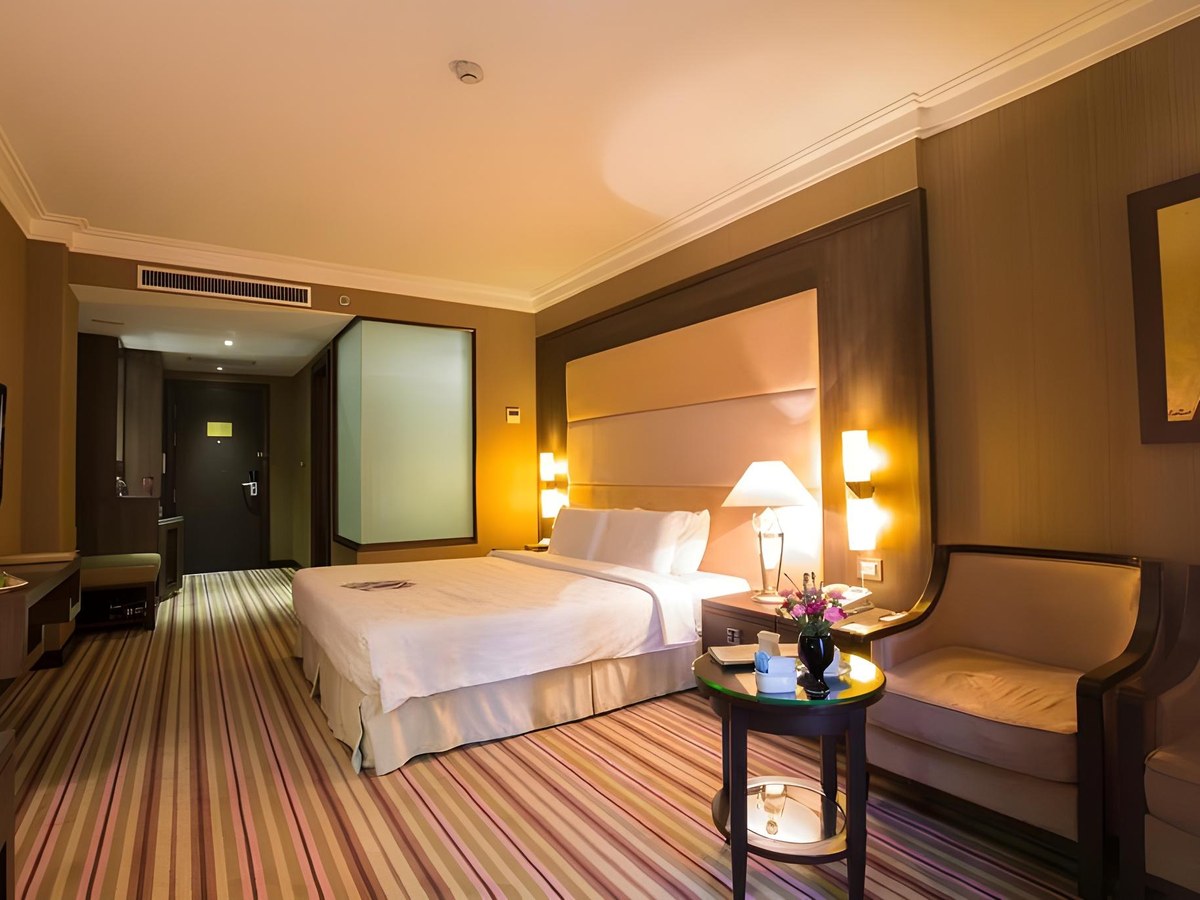 Premium Executive room with a king bed, a lounge chair and round table, dark wood walls and a frosted glass bathroom panel