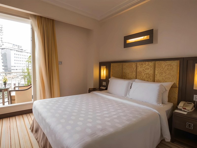 Executive room with a white king bed, gold-panelled headboard and an open glass door to a small balcony over the street