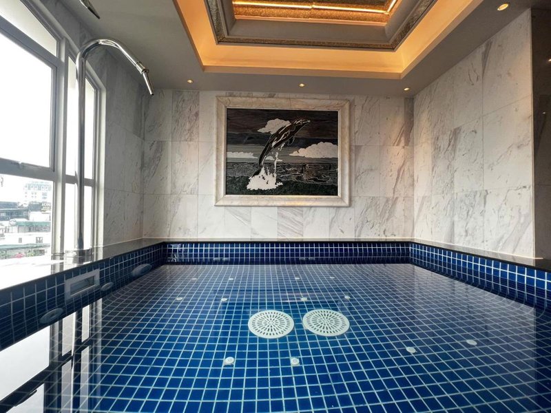 Indoor jacuzzi pool tiled in blue mosaic with two white circles, under a coffered ceiling with marble walls